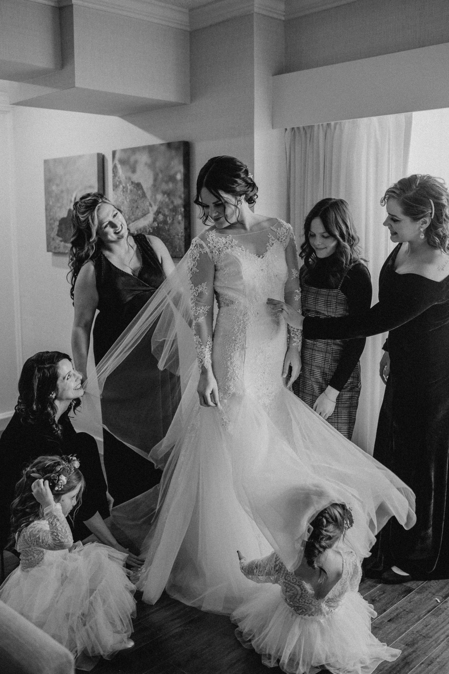 Black and white photo of bride and her bridal party fluffing her dress before her wedding ceremony.