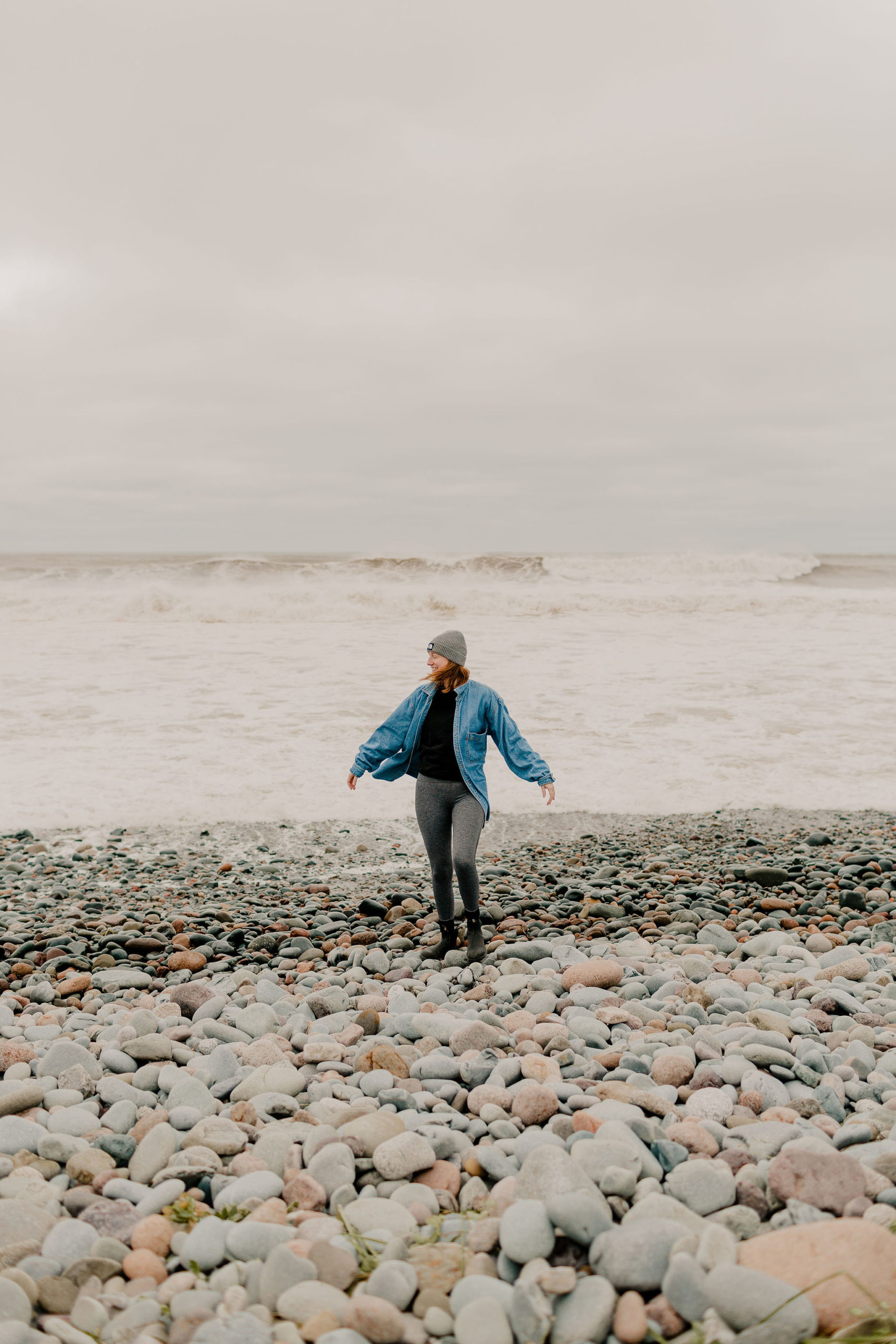 A woman spins on a rocky beach on a cloudy day.